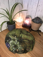 Load image into Gallery viewer, lifestyle photo of artisan round meditation floor cushion silk and merino wool with a floral pattern green with purple flowers there is a small plant a succulent and a selenite and amethyst crystal lamp
