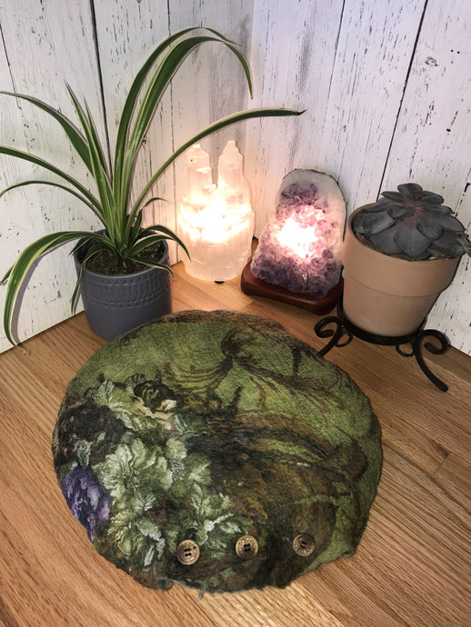 lifestyle photo of artisan round meditation floor cushion silk and merino wool with a floral pattern green with purple flowers there is a small plant a succulent and a selenite and amethyst crystal lamp