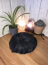 Load image into Gallery viewer, lifestyle photo of &quot; Twilight Awakening Meditation Cushion&quot; An artisan made round floor meditation cushion handmade with soft luxurious merino wool felted into silk fabric. Various shades of blues mixed with black and a hint of purple with a black shimmer. A small green plant succulent plant selenite tower lamp and amethyst crystal lamp in the background
